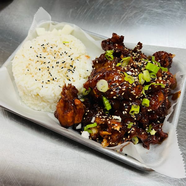 So-Ju Chikn' Korean fried chicken with dark sauce, sesame seeds, scallions, and white rice.