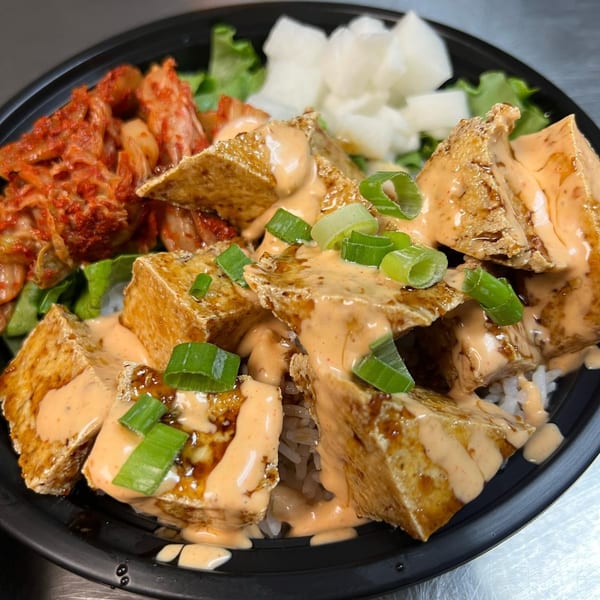 Korean tofu dish with spicy sauce, green onions, kimchi, and pickled radish in a black bowl.