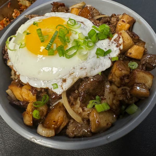 A Korean dish with meat, tofu, and a fried egg topped with green onions in a gray bowl.