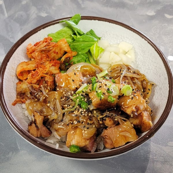 Korean chicken rice bowl with kimchi, greens, and pickled radish, garnished with sesame seeds.