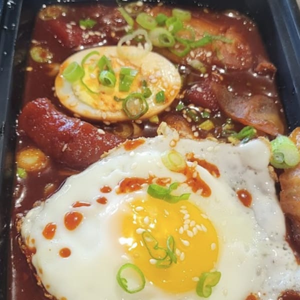Korean dish with a fried egg, a boiled egg, sausage, and meat in a rich red sauce.