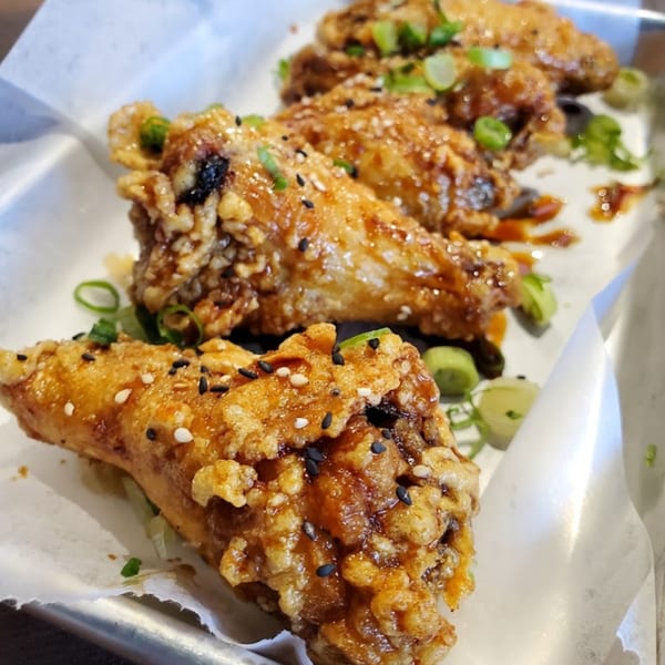 Crispy Korean fried chicken wings, glazed with sauce, sesame seeds, and green onions on parchment paper.