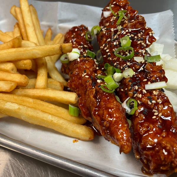 So-Ju Chikn' Korean fried chicken tenders with sweet and spicy sauce, sesame seeds, scallions, and fries.