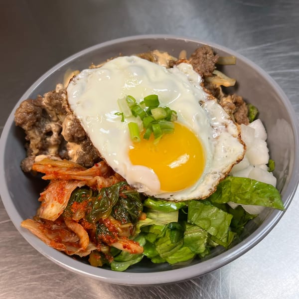 Korean bibimbap bowl with bulgogi, kimchi, fresh lettuce, pickled radish, and a fried egg.