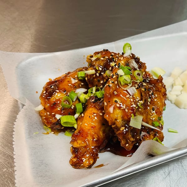 Korean fried chicken wings, glazed with sauce, sesame seeds, and green onions, with pickled radish.
