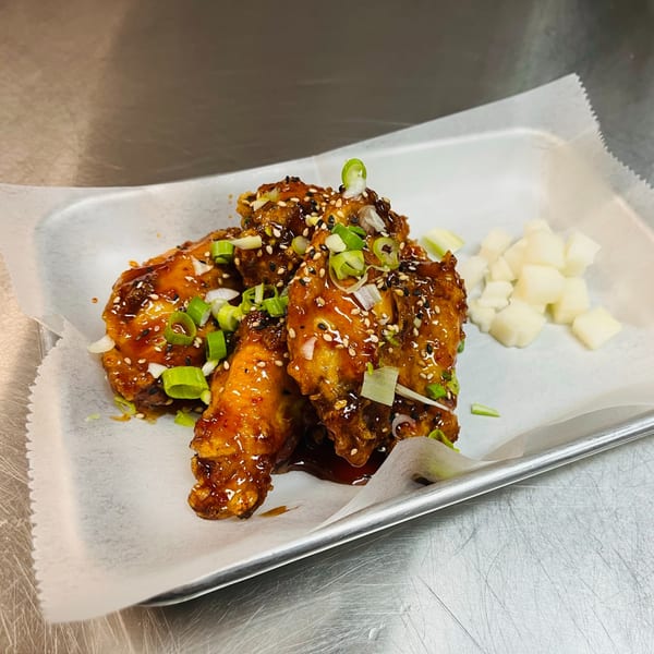 Korean fried chicken wings with sauce, sesame seeds, green onions, and pickled radish on a tray.