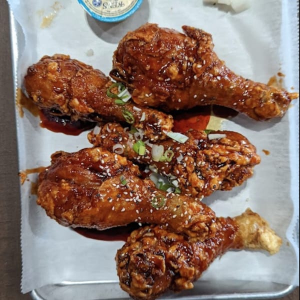 Four pieces of So-Ju Chikn' Korean fried chicken drumsticks, glazed with sauce, sesame seeds, and green onions.