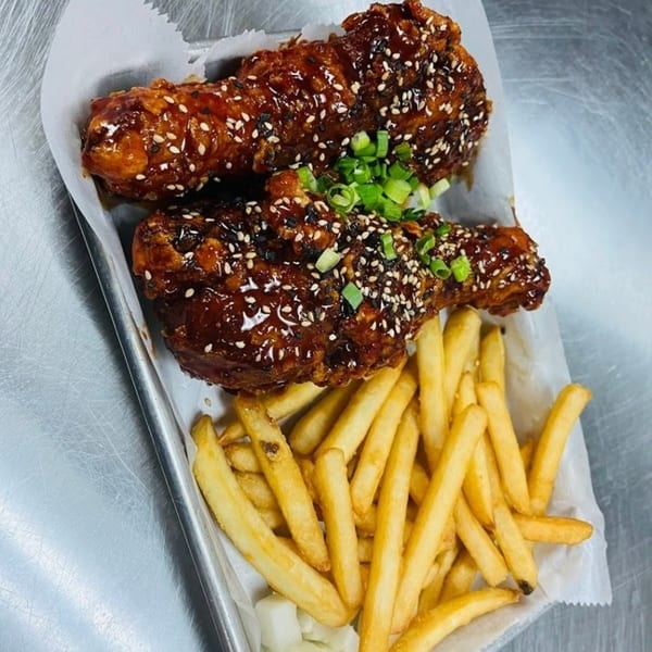 Two Korean fried chicken drumsticks with sesame seeds and scallions, served with golden french fries.
