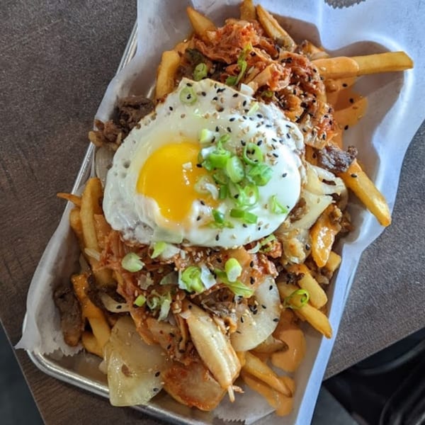 So-Ju Chikn's kimchi fries topped with bulgogi, a fried egg, green onions, and sesame seeds.